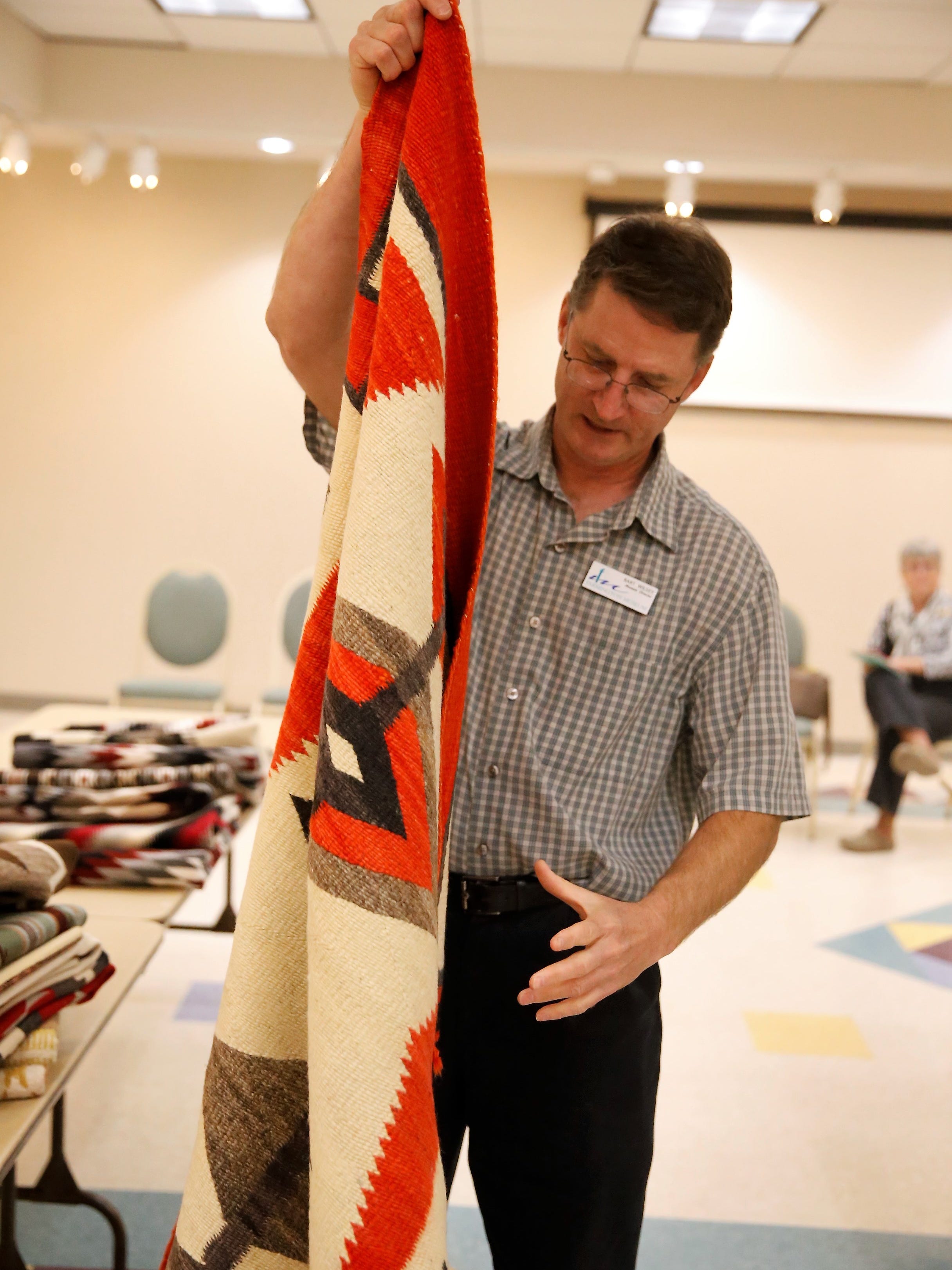Farmington Museum director Bart Wilsey folds one of the weavings included in the annual Navajo Benefit Rug Auction taking place Saturday at the museum.